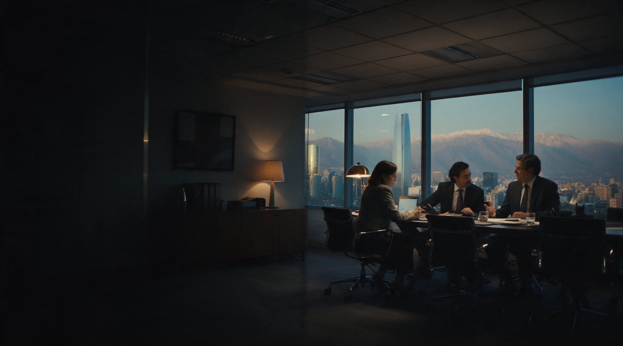 Ejecutivos reunidos en una oficina al atardecer, con el skyline de Santiago y la cordillera de los Andes tras los ventanales.